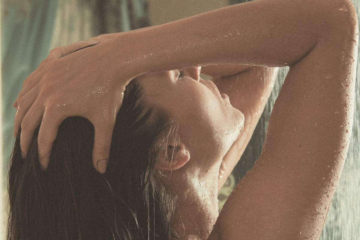 Femme sous la douche, les mains dans ses cheveux mouillés : l'eau du robinet agit sur les cheveux et la peau